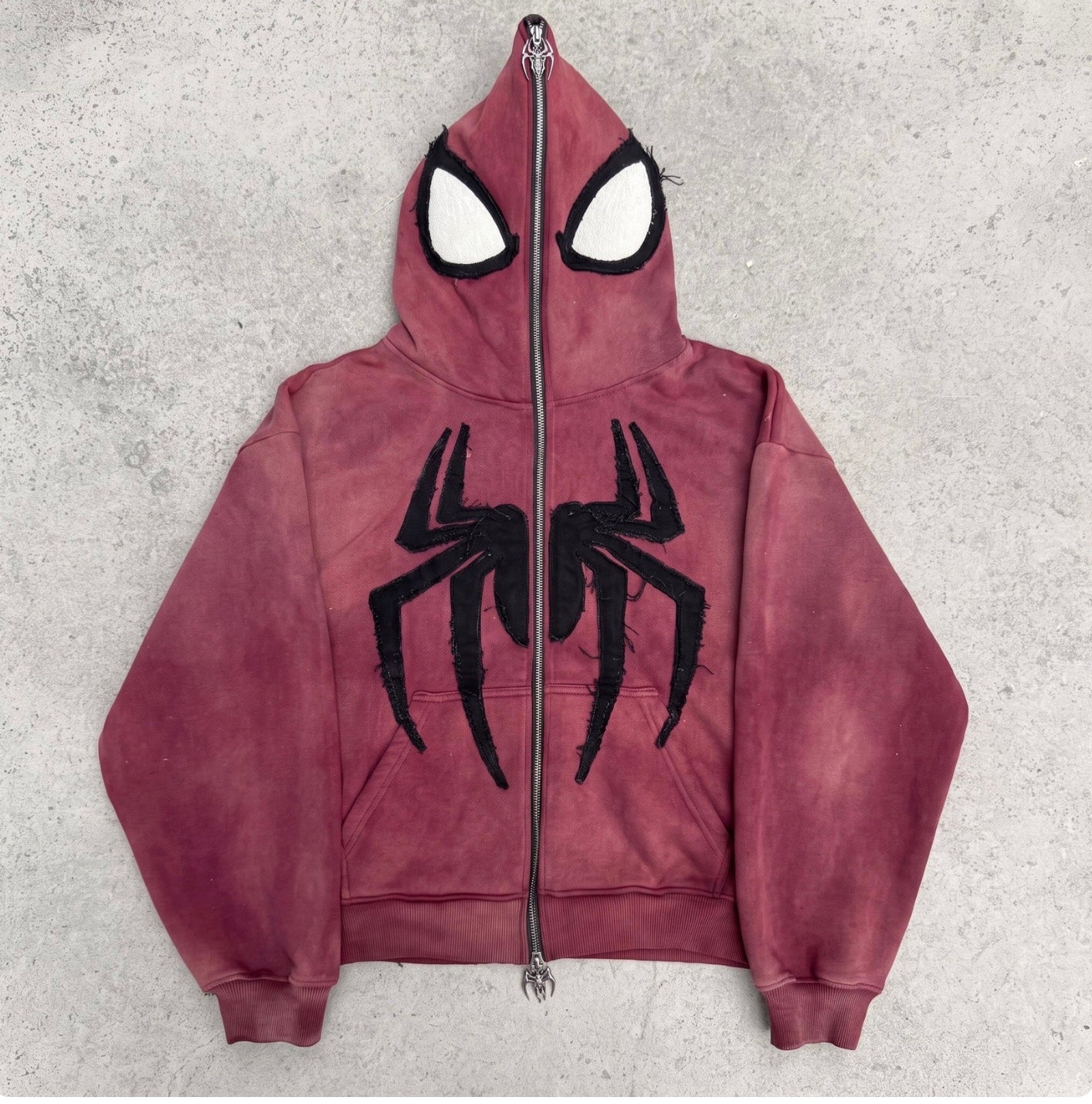 Faded Crimson full-face zip hoodie laid flat on concrete with the hood zipped shut into a mask