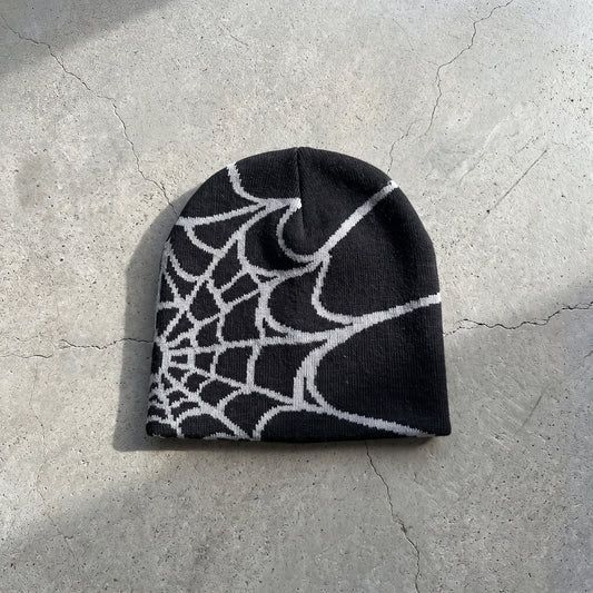 Black spider web knit beanie with ash grey web on raw concrete