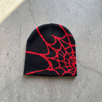 Black spider web knit beanie with crimson web on raw concrete