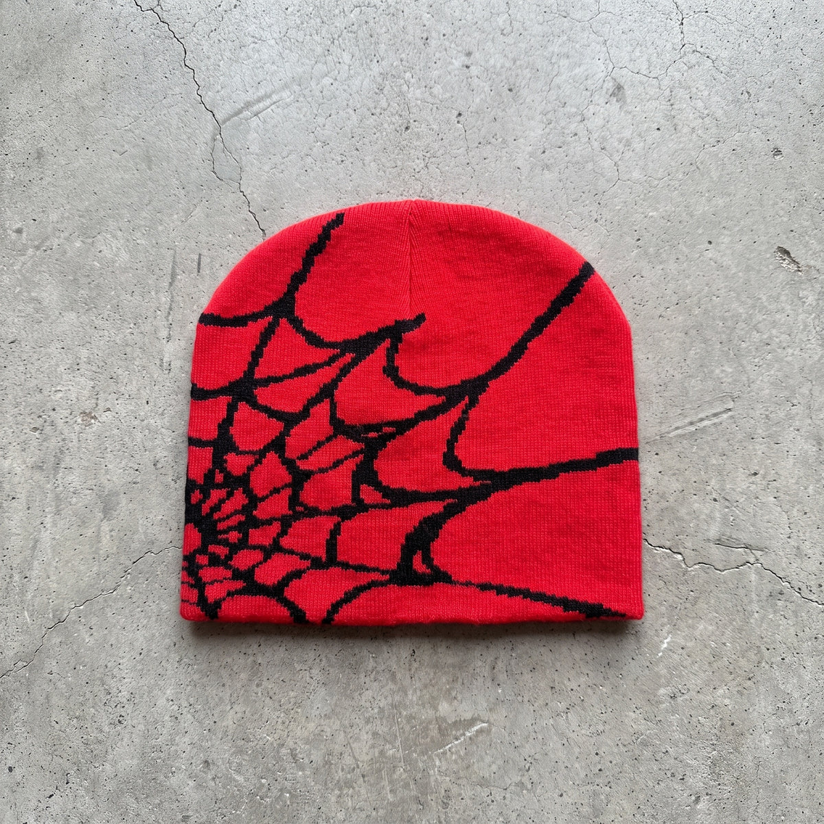 Crimson spider web knit beanie with black web on raw concrete