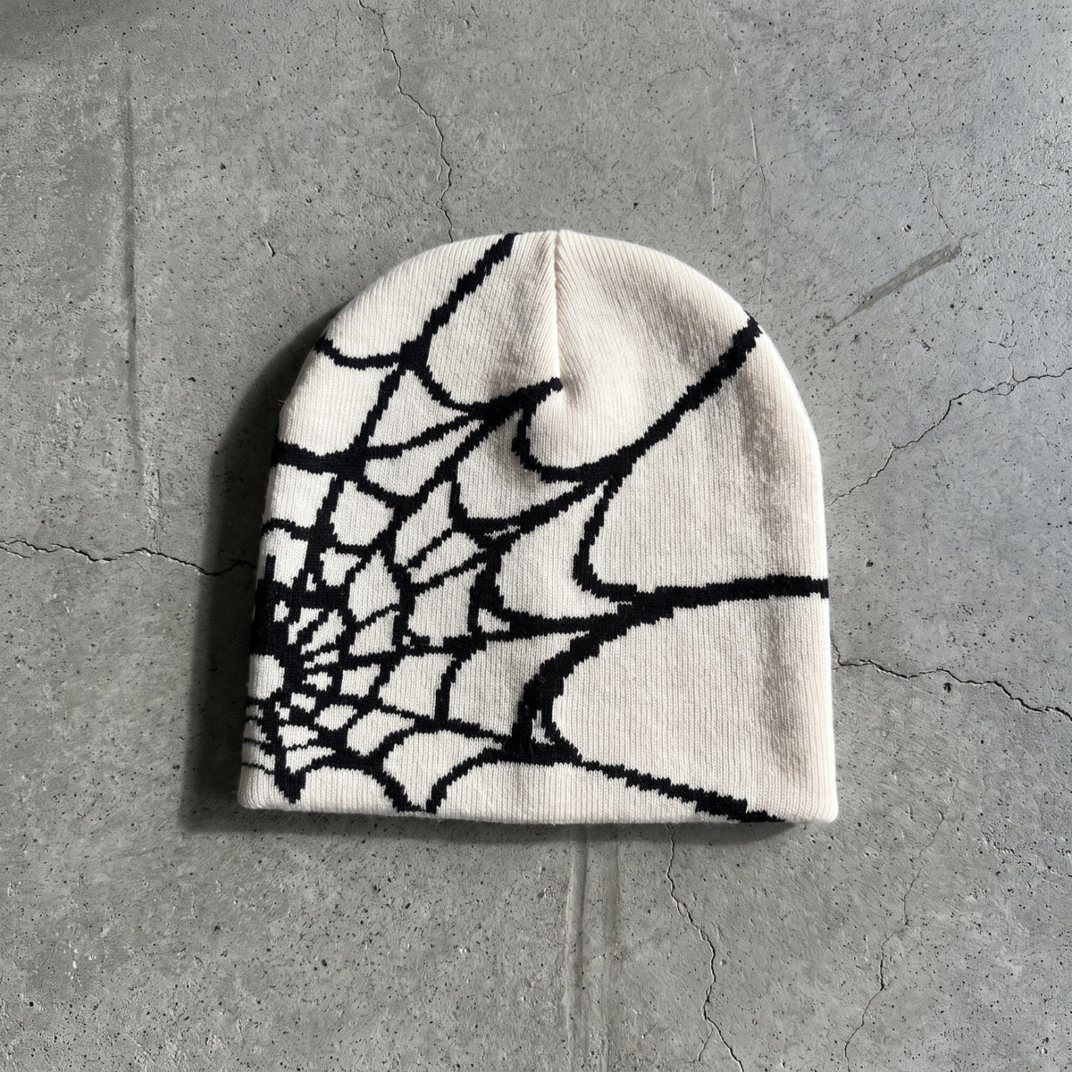 Bone white spider web knit beanie with black web on raw concrete