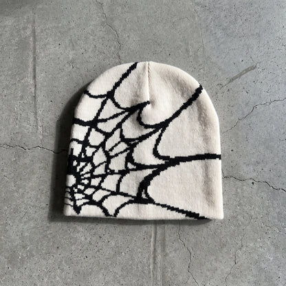 Bone white spider web knit beanie with black web on raw concrete