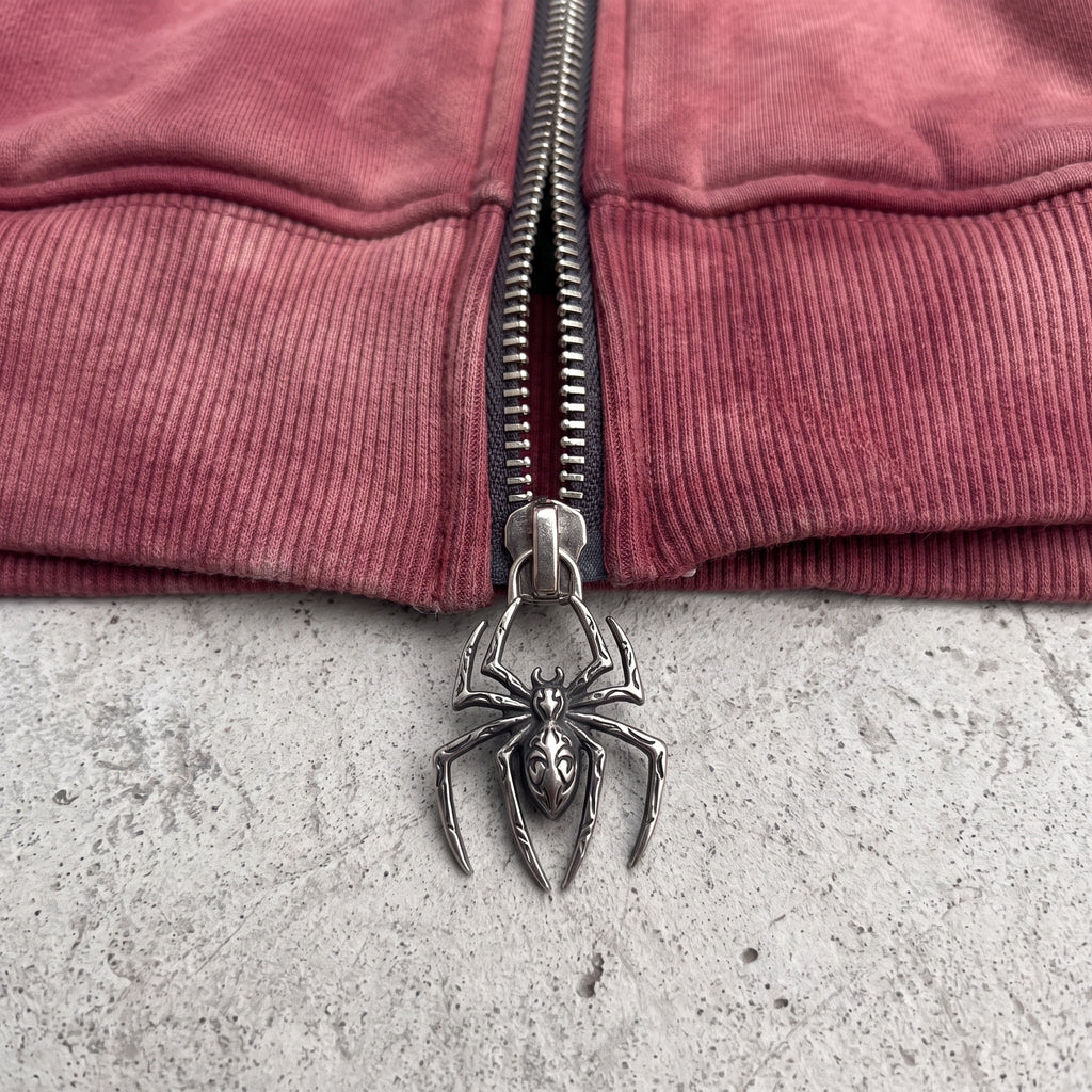 Macro of the cast-metal spider zipper pull at the ribbed hem