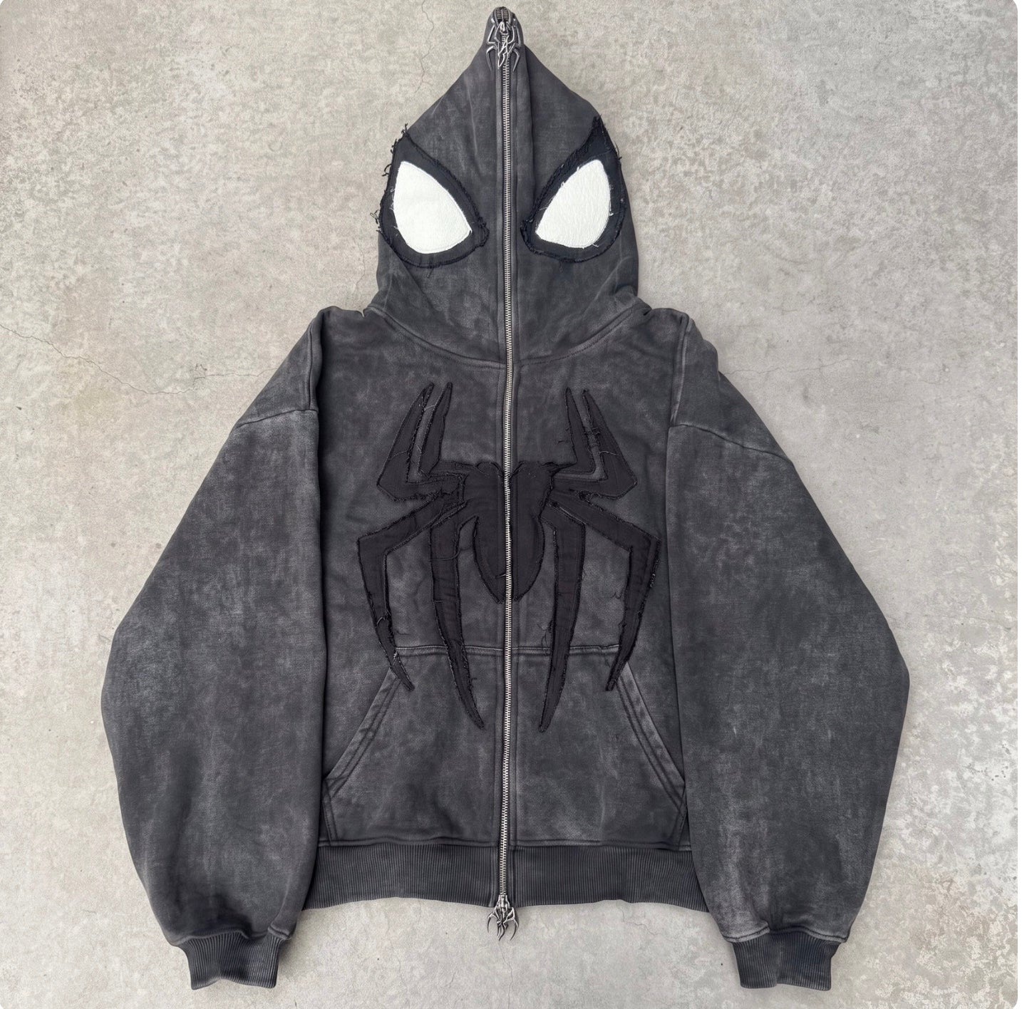 Washed Black full-face zip hoodie laid flat on concrete with the hood zipped shut into a mask