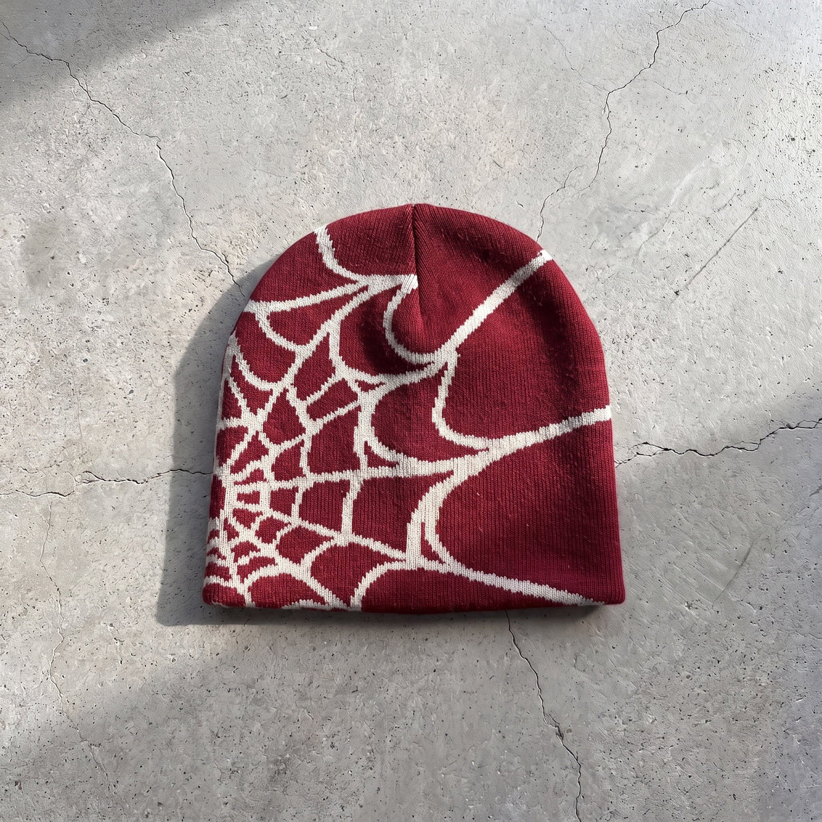 Crimson web knit beanie with bone white web on raw concrete