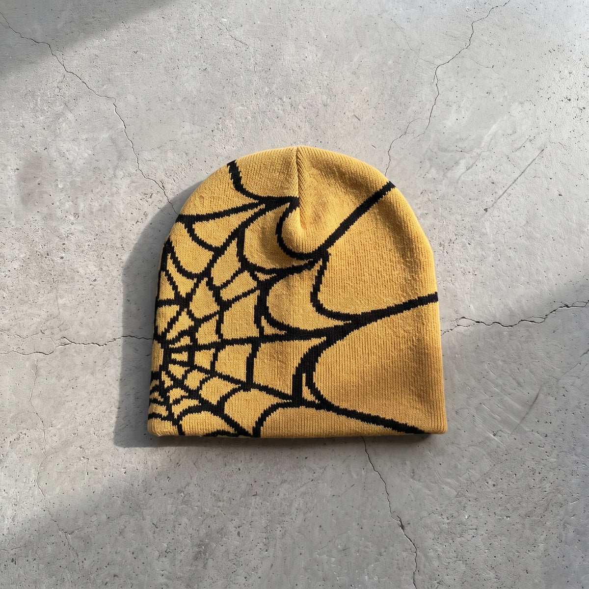 Gold yellow web knit beanie with black web on raw concrete