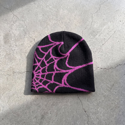 Black web knit beanie with magenta web on raw concrete
