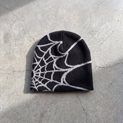 Black web knit beanie with bone white web on raw concrete