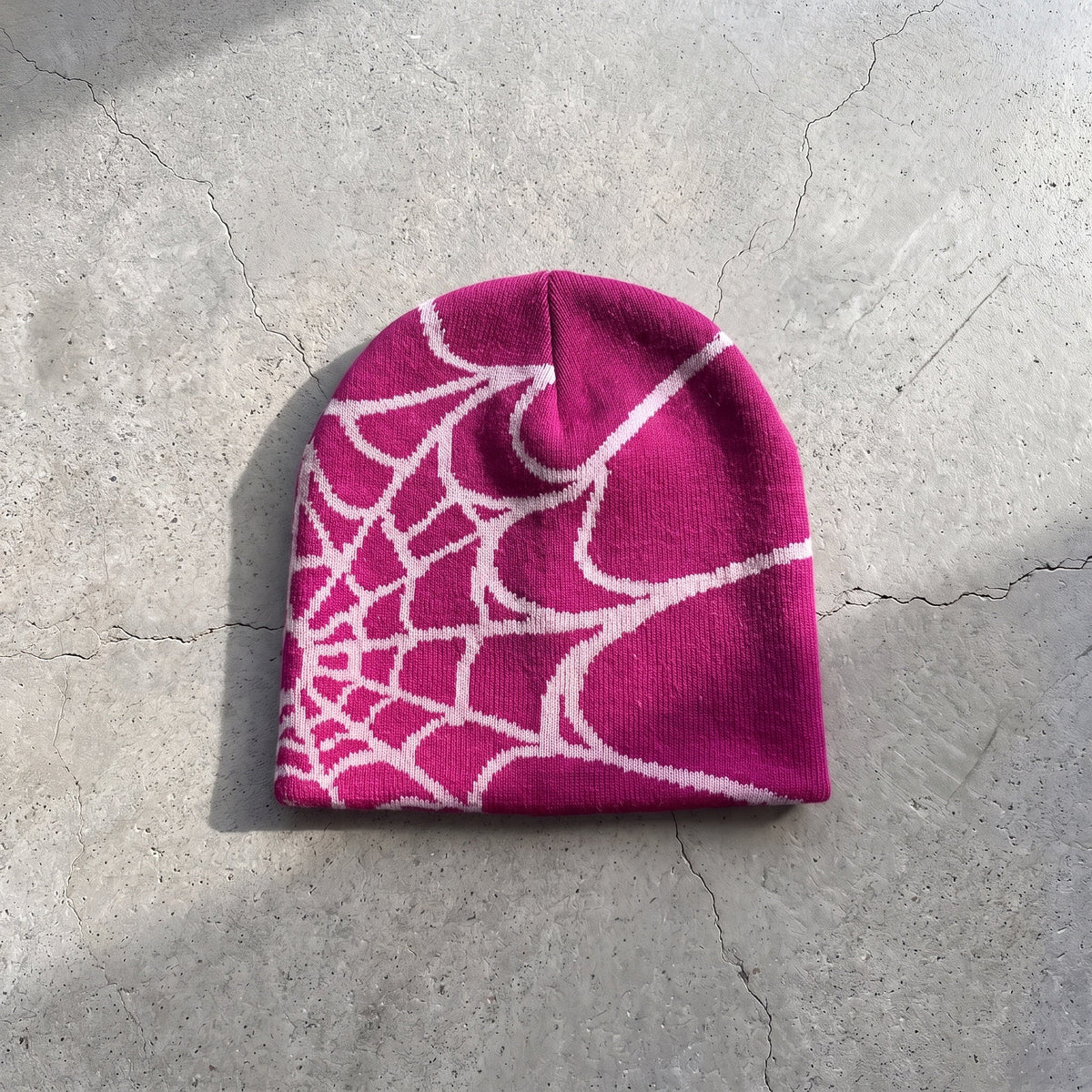 Magenta web knit beanie with pale pink web on raw concrete