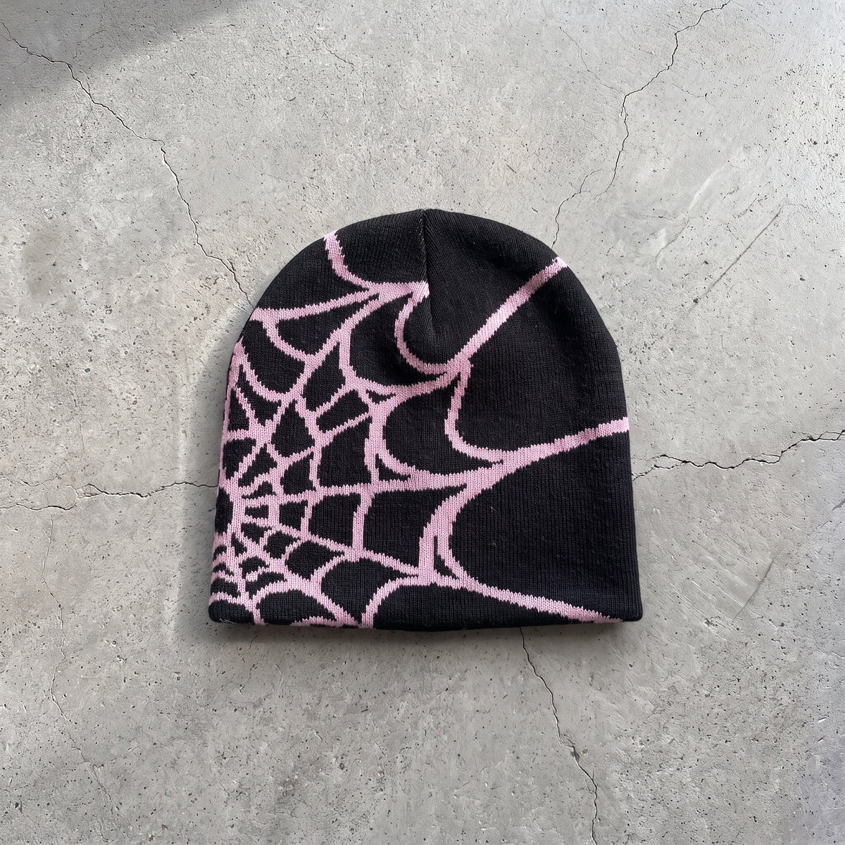Black web knit beanie with soft pink web on raw concrete