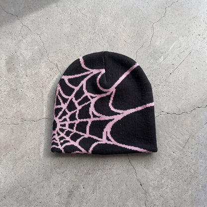 Black web knit beanie with soft pink web on raw concrete